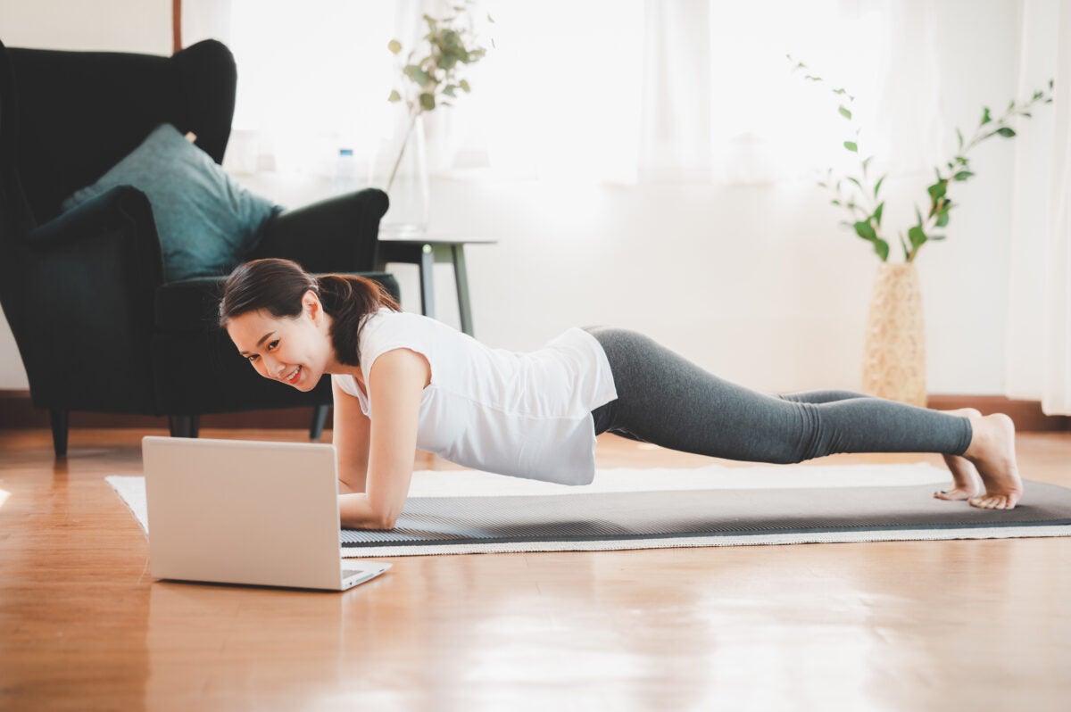 woman doing plank exercise at home while watching online workout session from laptop